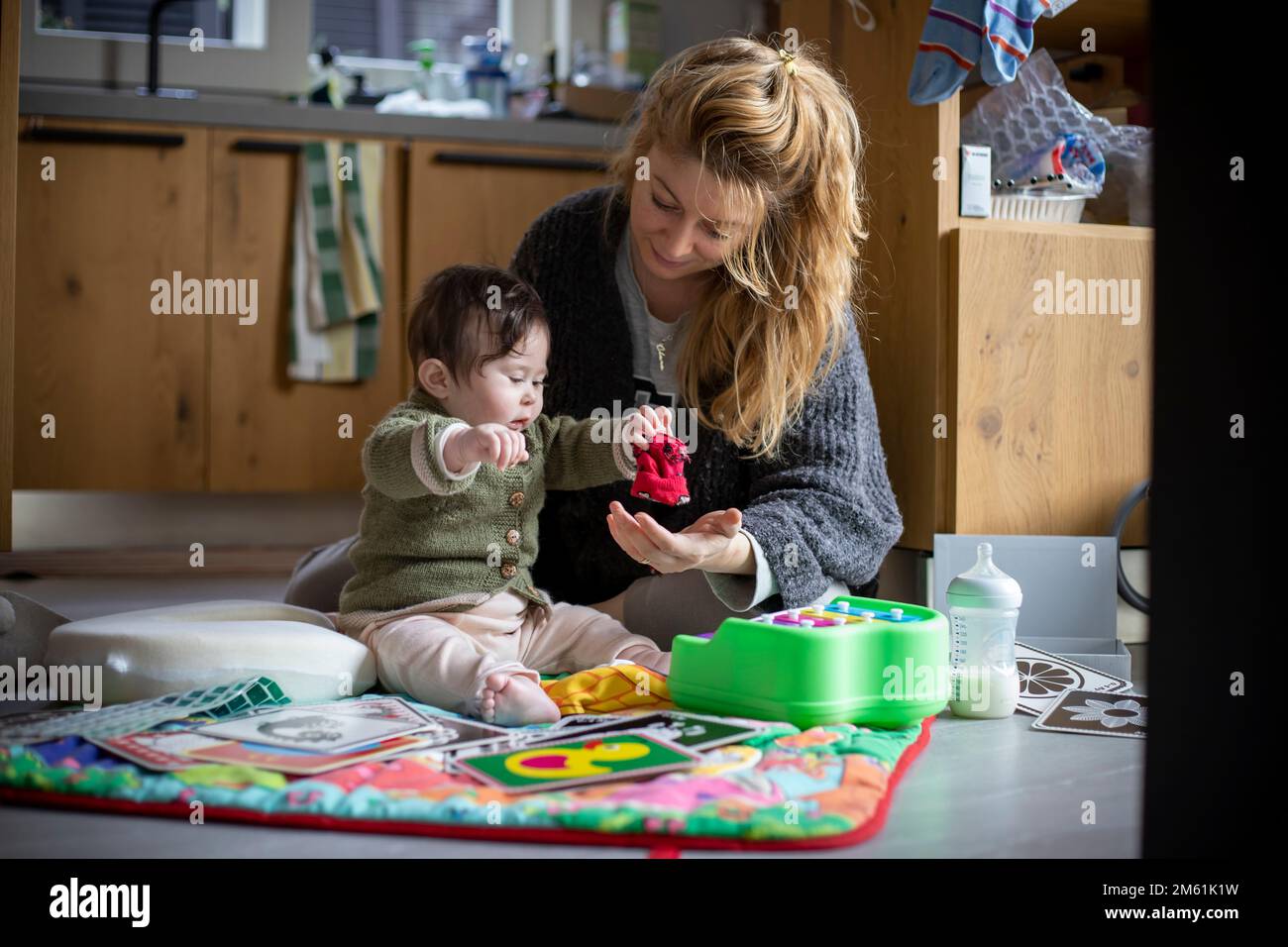Young mother playing with her baby girl on the play rug laid out on the floor of the messy house in the morning with home clothes.Daily lifestyle. Stock Photo