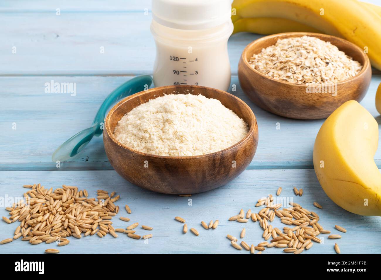 Powdered milk and oatmeal, banana baby food mix, infant formula, pacifier, bottle, spoon on blue wooden background. Side view, artificial feeding conc Stock Photo