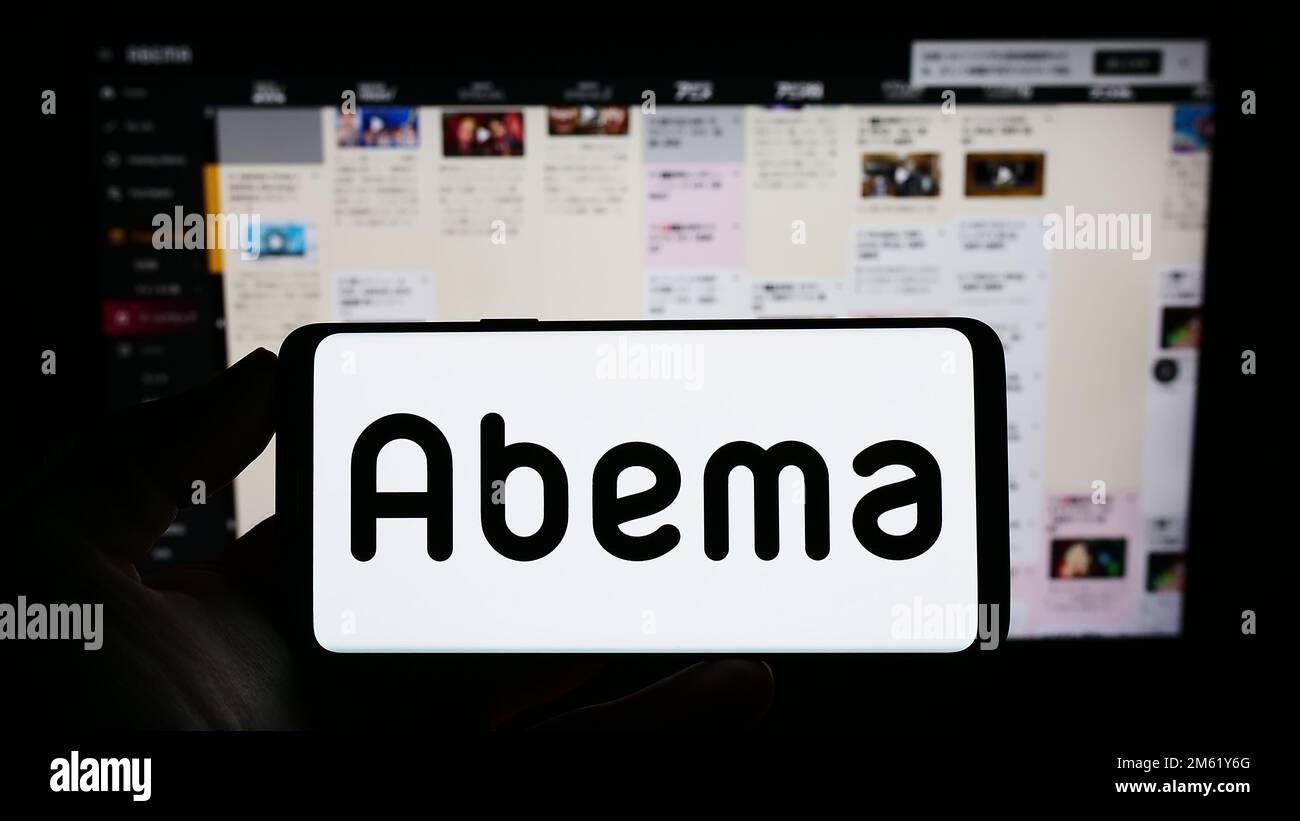 Person holding mobile phone with logo of Japanese streaming company AbemaTV Inc. (Abema) on screen in front of web page. Focus on phone display. Stock Photo