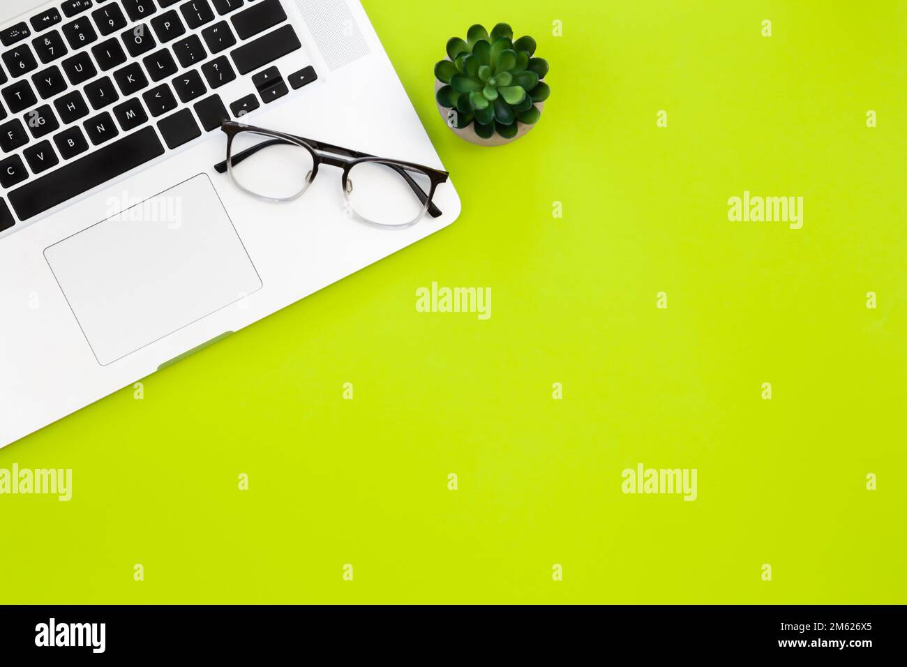 Laptop and glasses on a green background, flat lay. Stock Photo