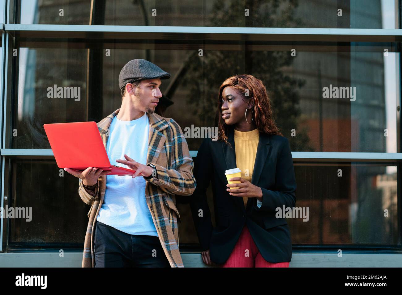 Colleagues using a laptop and talking about work while standing outside the office building. Stock Photo