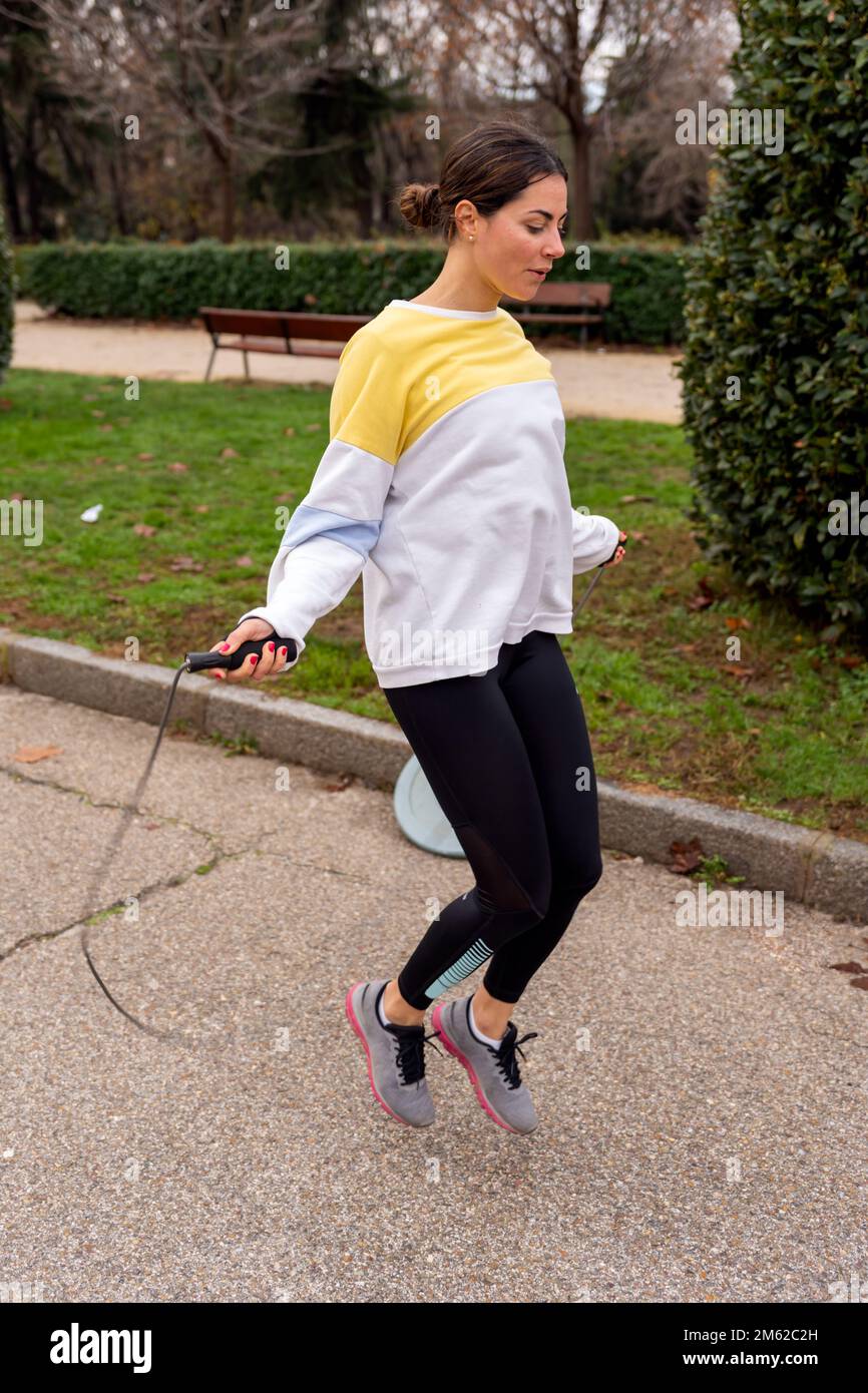 Full body of lady in sportswear and sneakers exercising with skipping rope on path in summer park Stock Photo