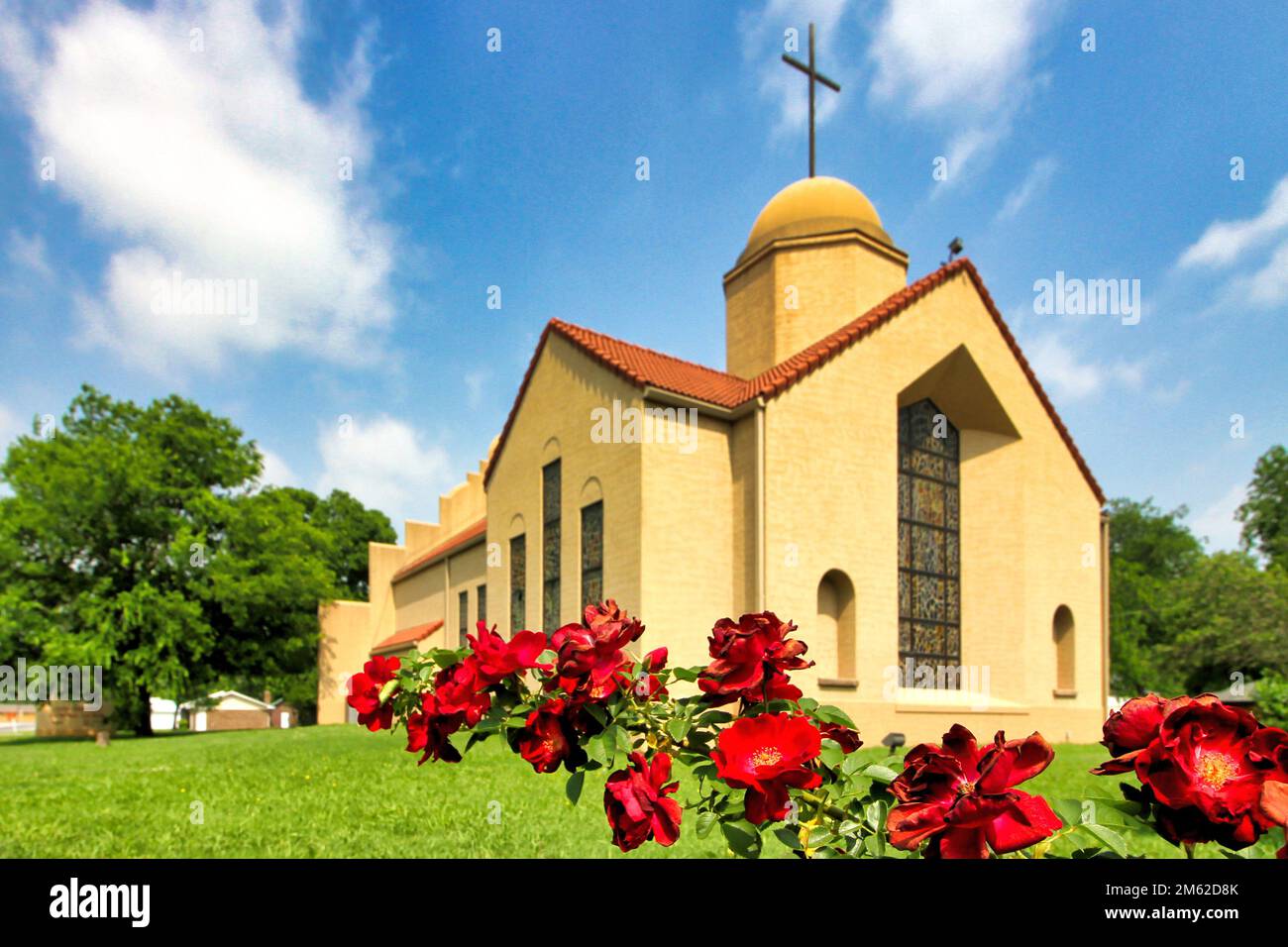The modern Mission Revival style Good Shepherd Catholic Mission church in Marietta Oklahoma with a branch of red roses in front. Stock Photo
