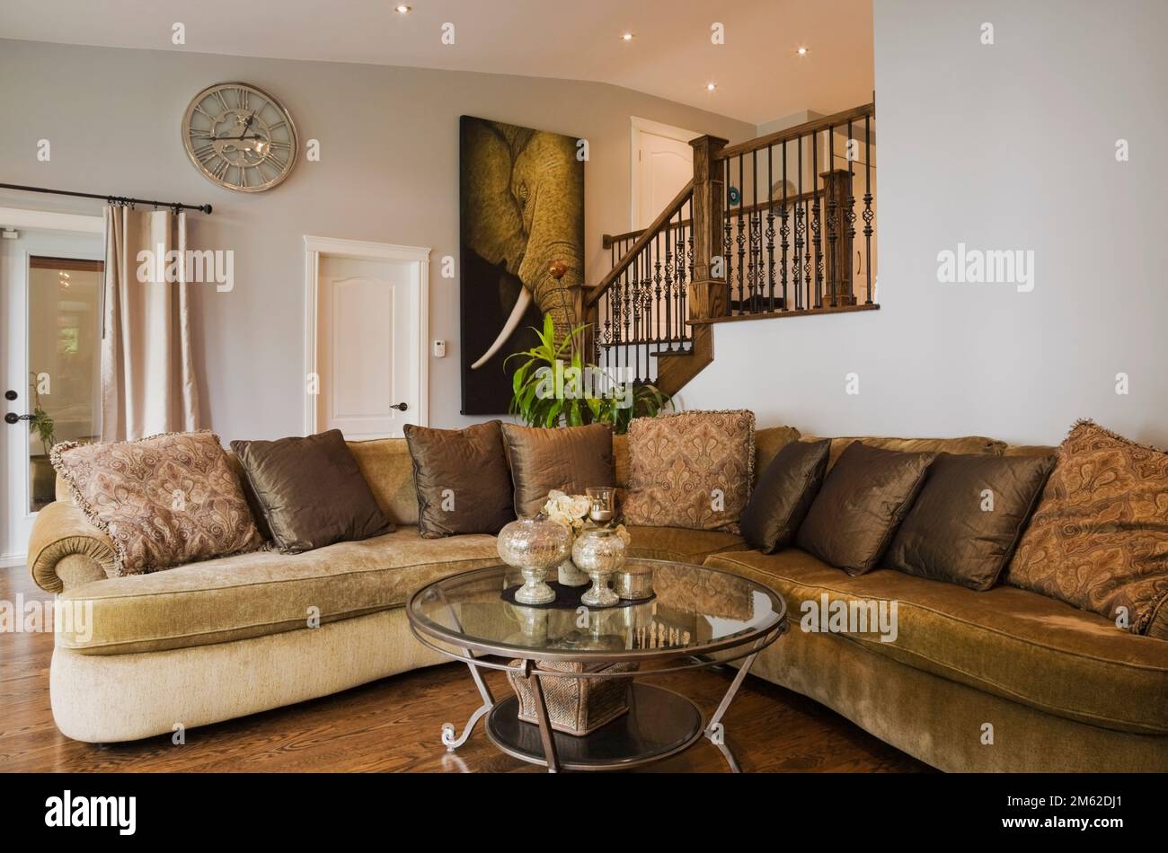 L-shaped beige and tan upholstered sofa and round glass coffee table in living room inside luxurious home. Stock Photo