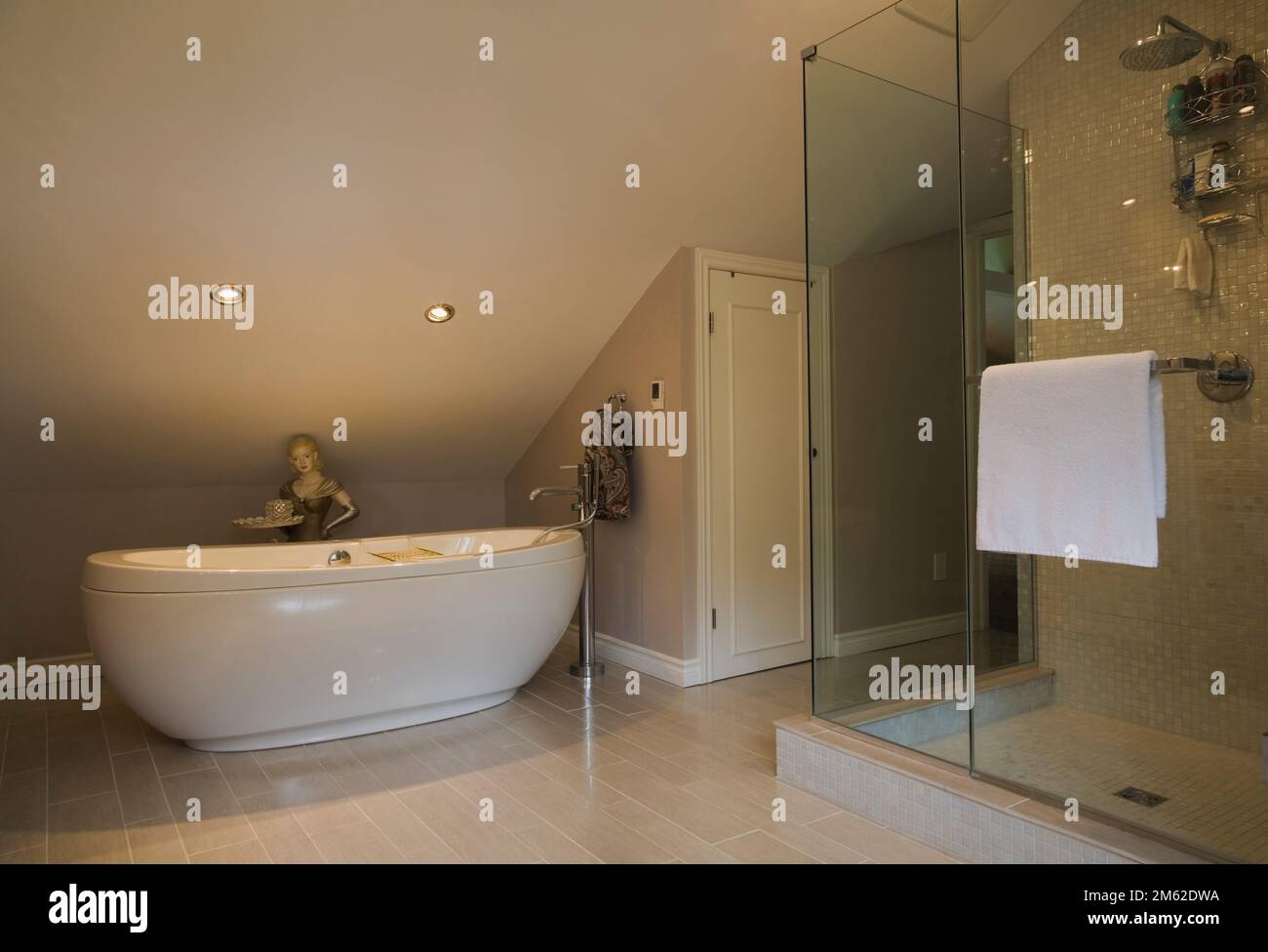 Oval shaped freestanding bathtub and glass shower stall in spacious ensuite inside luxurious home. Stock Photo