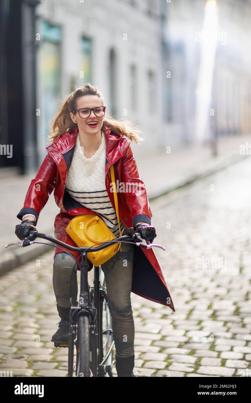 smiling modern woman in red rain coat outside on the city street riding ...