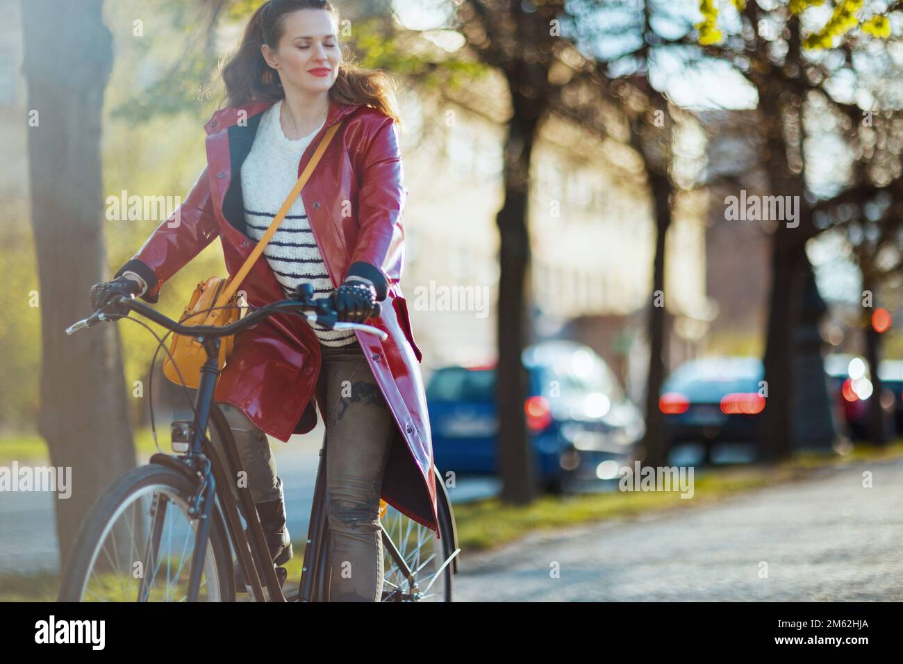 relaxed modern woman in red rain coat outside on the city street riding ...