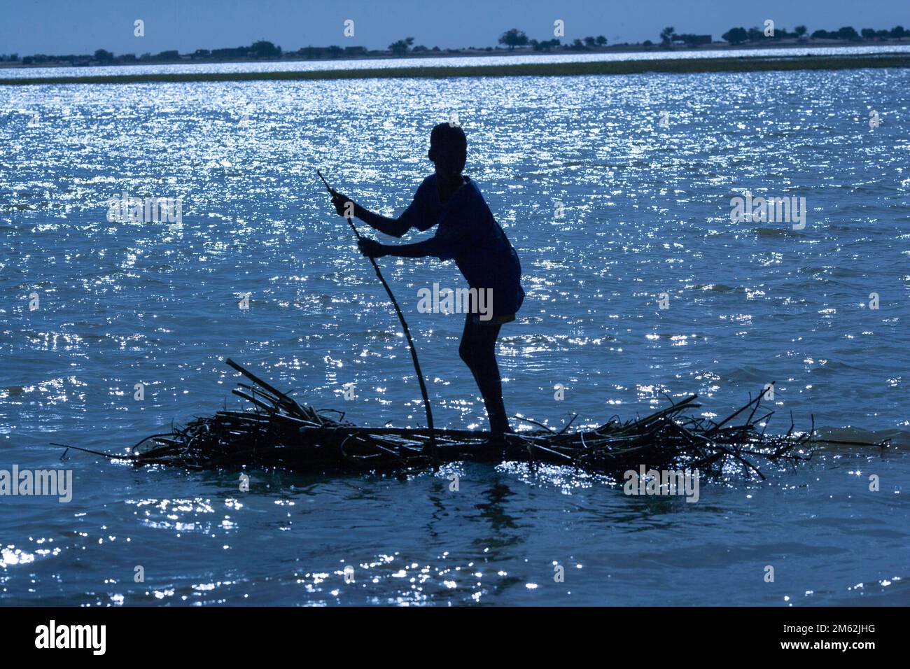 sunset shilouette of boy standing on his raft made out of sticks ...