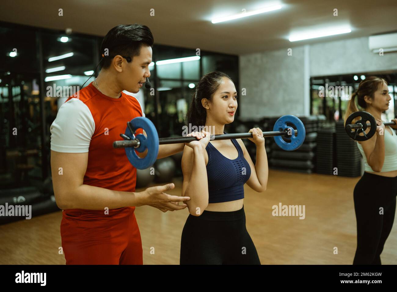 instructor instructs young woman on proper movements using a barbell Stock Photo