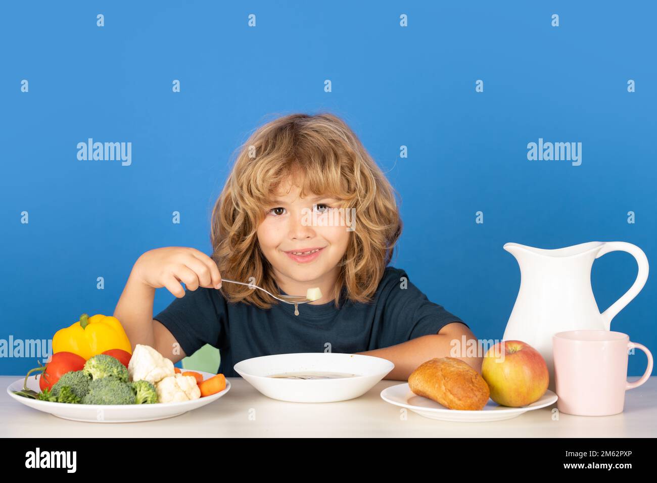 Child eating soup. Child eating healthy food at kithen. Baby eat soup with spoon. Stock Photo