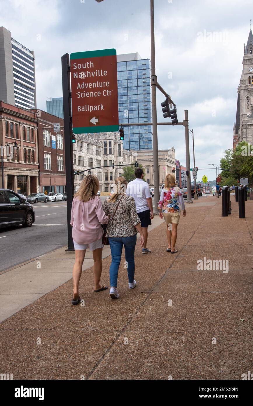 Tourists walking on sidewalk in downtown Nashville, Tennessee, past sign with arrow that reads South Nashville, Adventure Science Center, Ball Park. Stock Photo