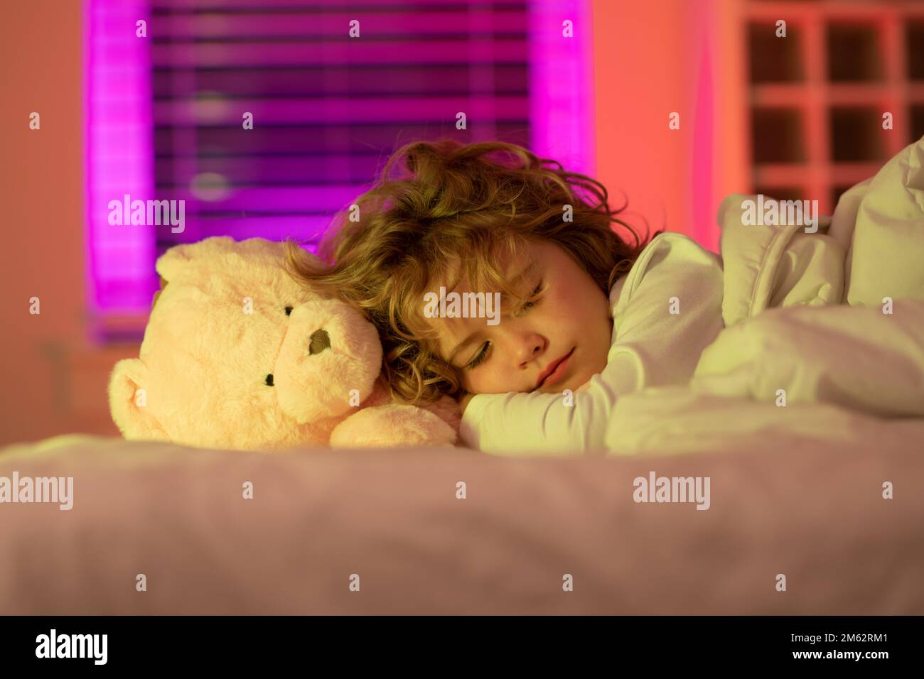 Kid enjoying sweet dreams. Kid sleeping with a toy teddy bear in bed