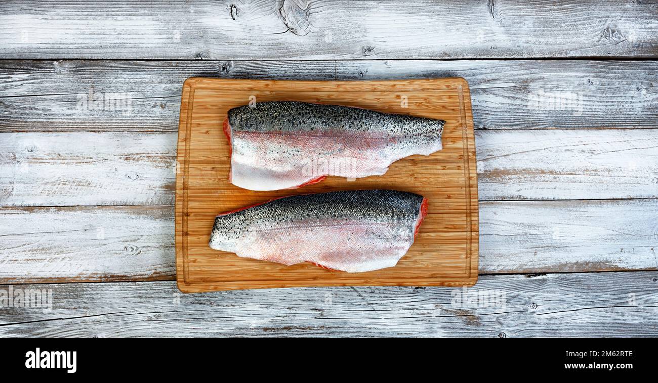 Two fillet, skin side up, of trout salmon on cutting board with white rustic wooden table background Stock Photo