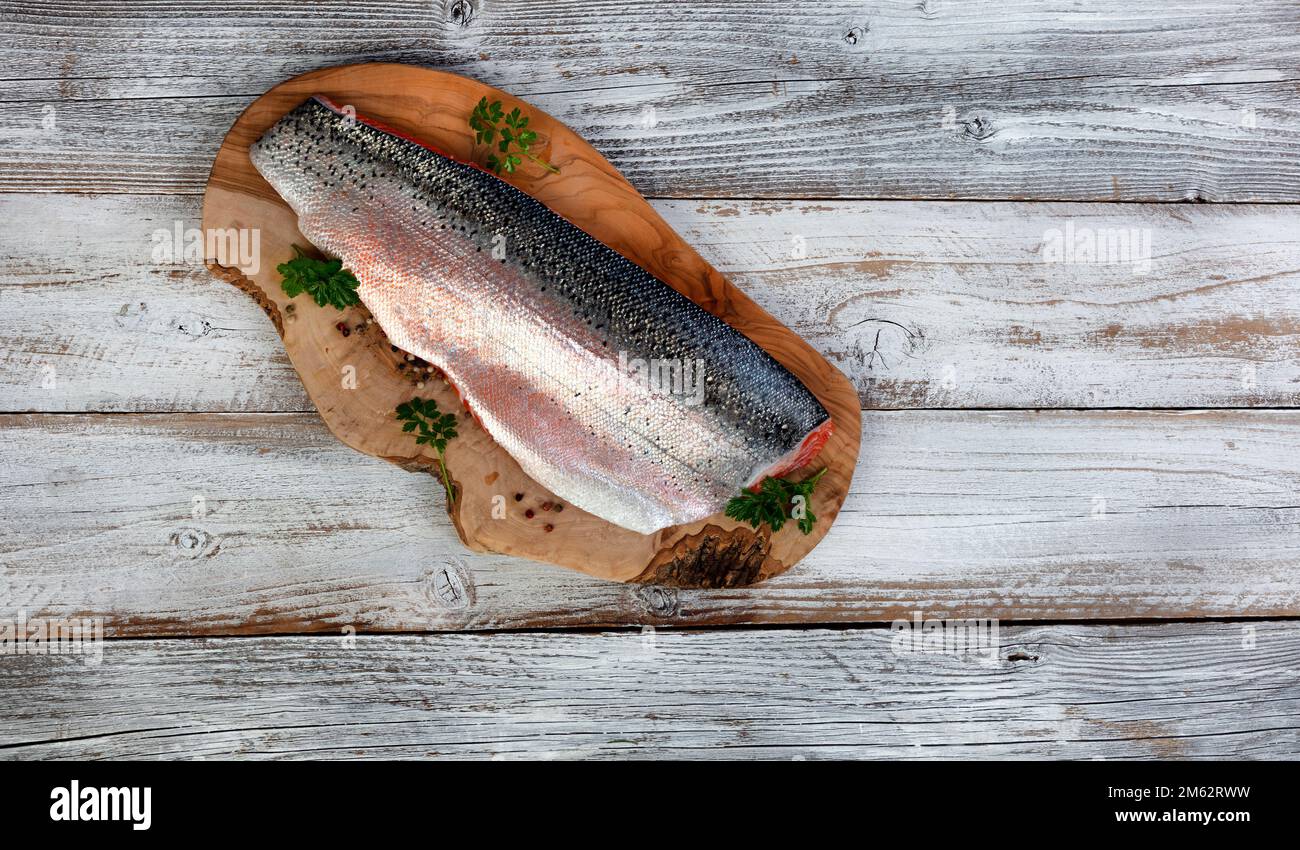 Salmon trout fillet, skin side up, on olive wood board with white rustic wooden table background Stock Photo