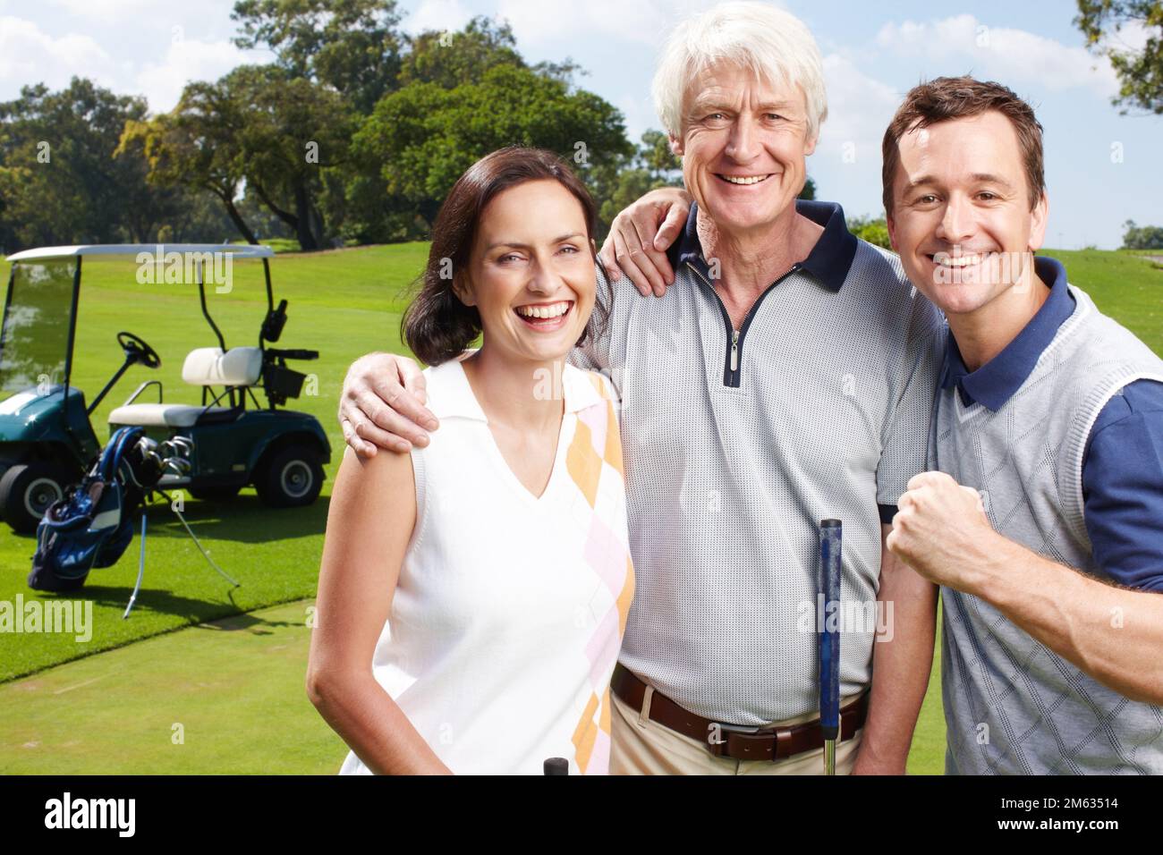 Family day on the green. Smiling golfing companions on the green with their golf cart in the background. Stock Photo