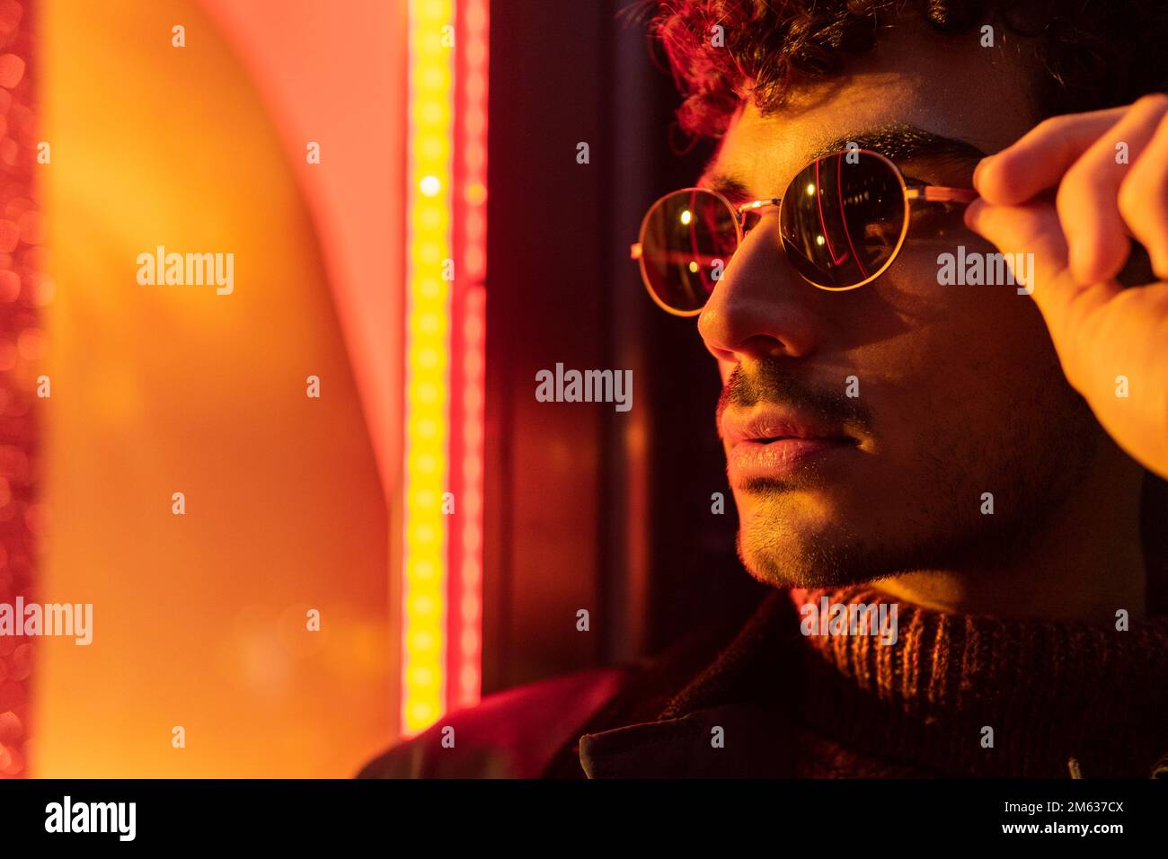 Pondering ethnic guy with curly hair in round glasses looking out window in  dark room Stock Photo - Alamy