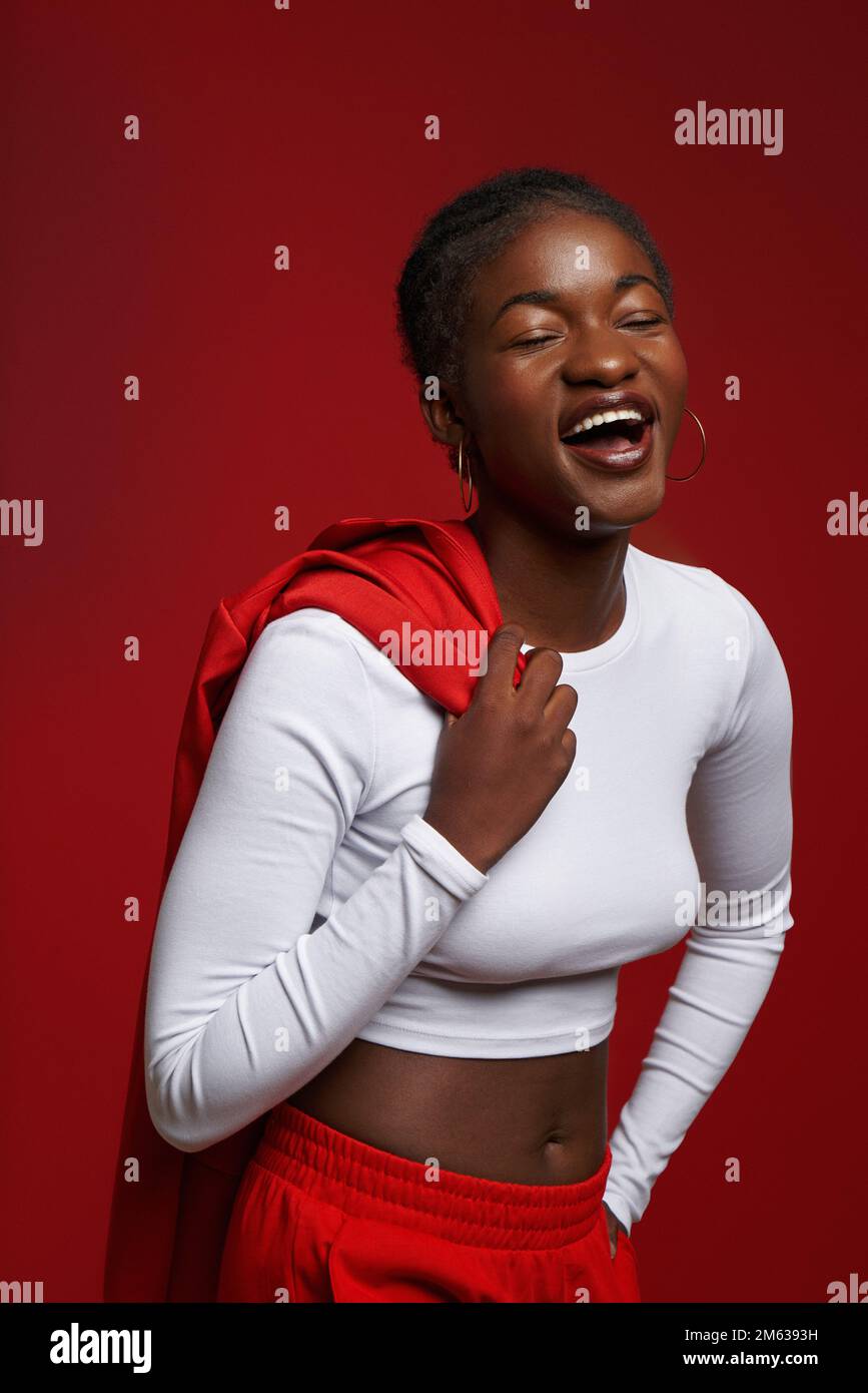 Happy black woman with dark hair holding red jacket on shoulder against red background Stock Photo