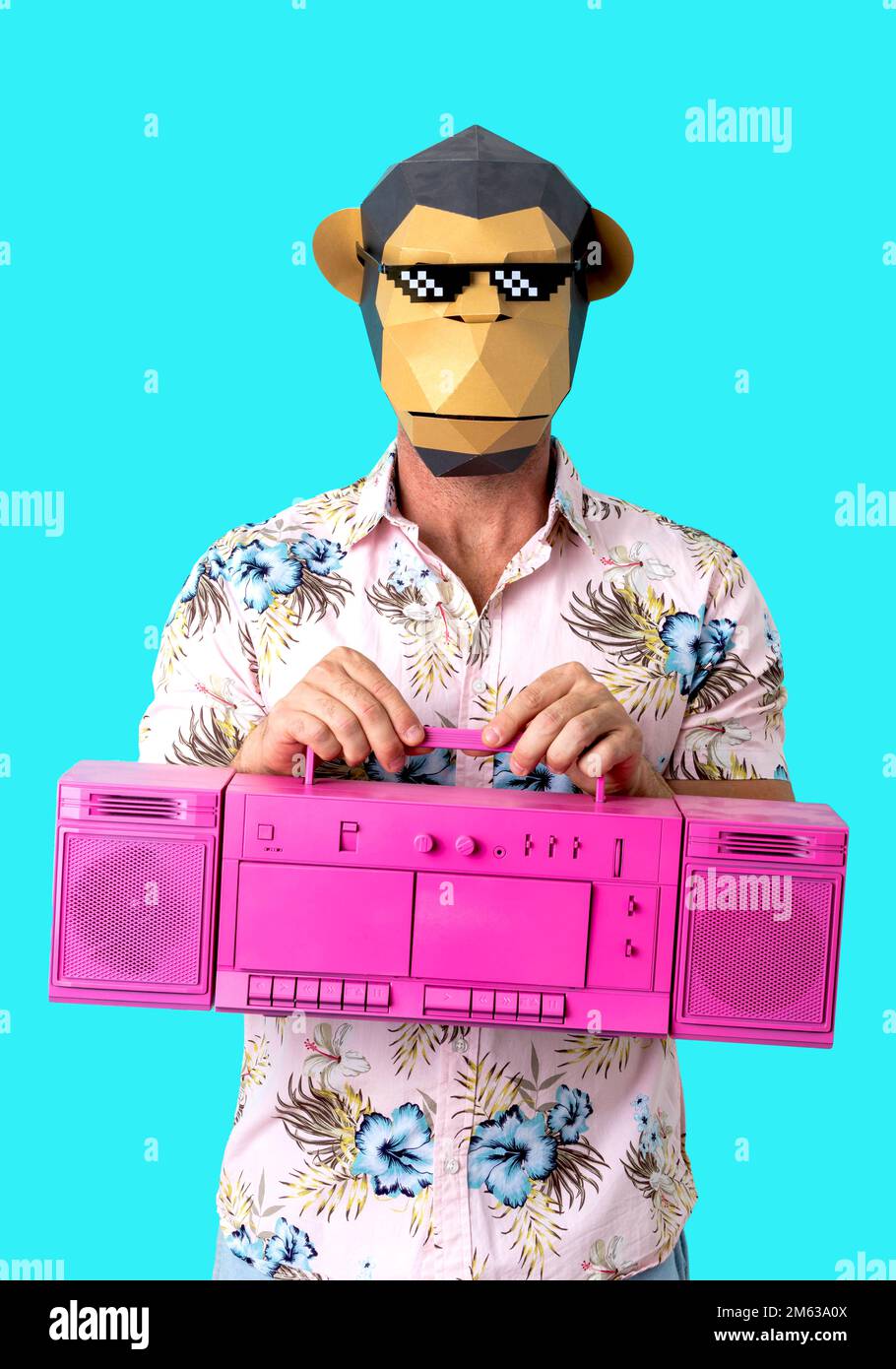 Unrecognizable male model in pixel monkey mask and summer shirt holding retro bright pink tape recorder against blue background Stock Photo
