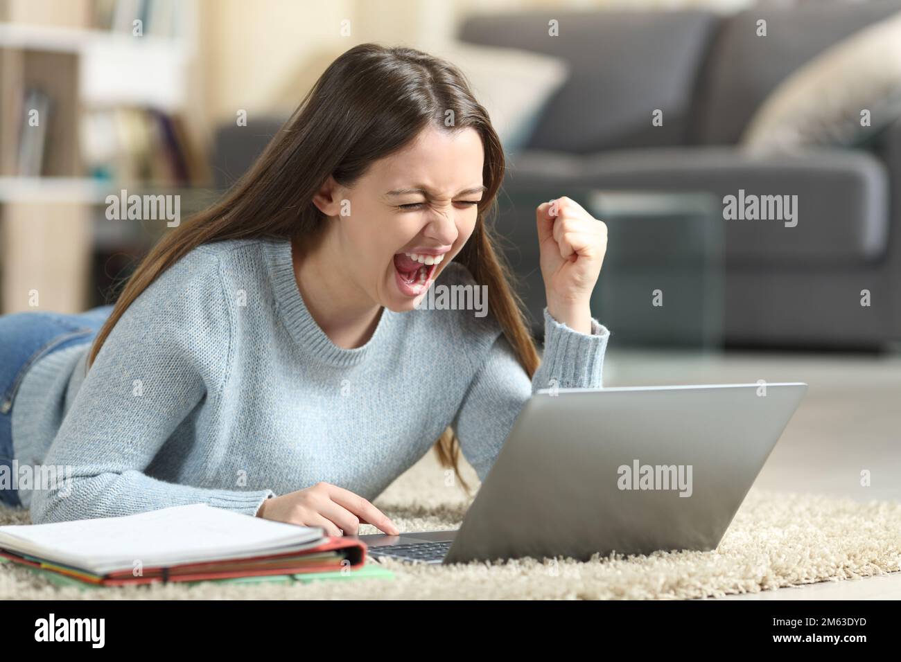 Excited student lying on the floor checking laptop at home Stock Photo