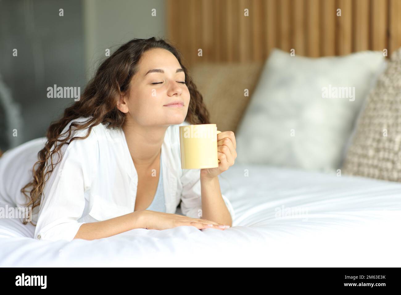Happy woman lying on a bed enjoying a cup of coffee Stock Photo Alamy