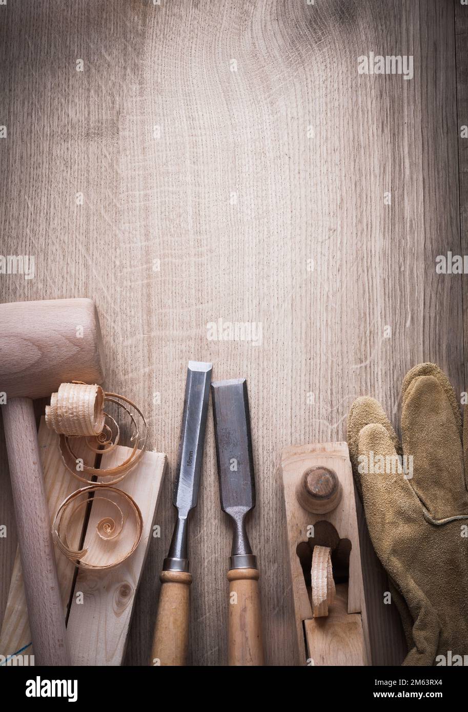 Wooden bricks hammer curled up scobs planer firmer chisels leather gloves on wood background construction concept. Stock Photo