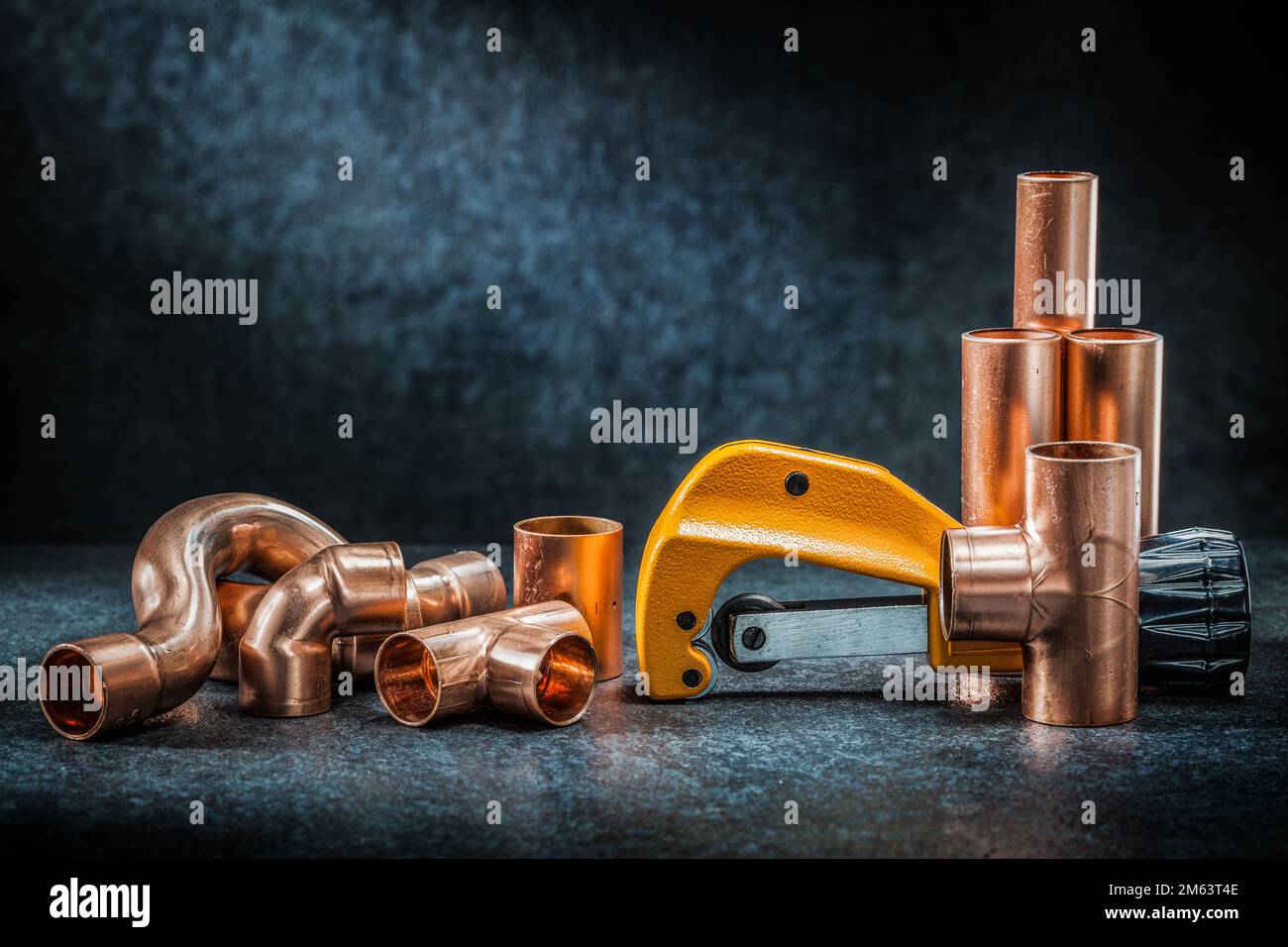 yellow pipe cutter and copper pipe with connectors on dark background Stock Photo