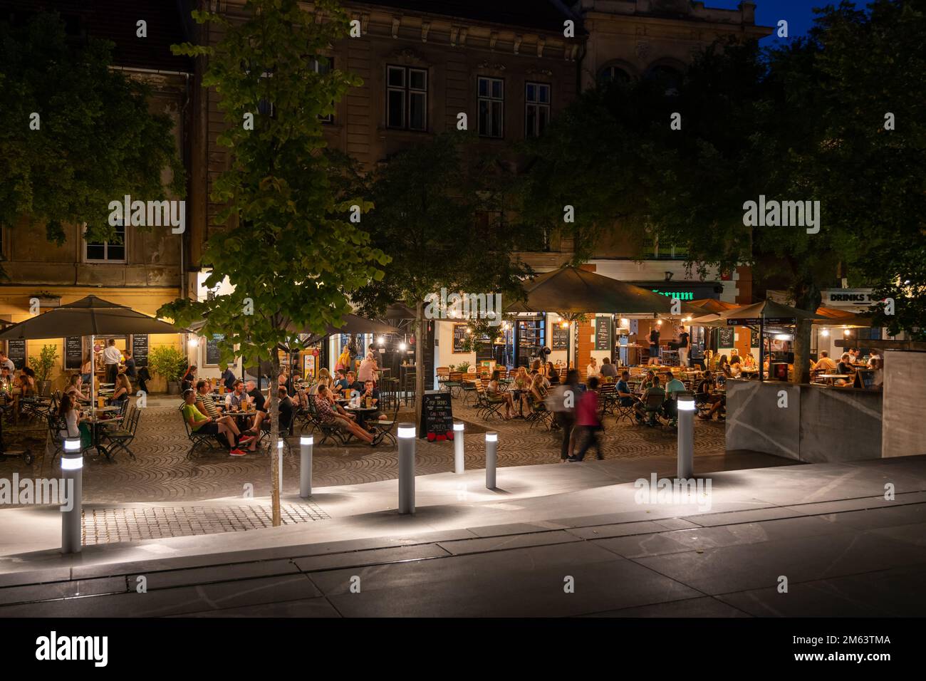 Ljubljana, Slovenia - July 14, 2022: Group of people at restaurant tables enjoying the summer evening meal on Petkovskovo Nabrezje riverside at night, Stock Photo