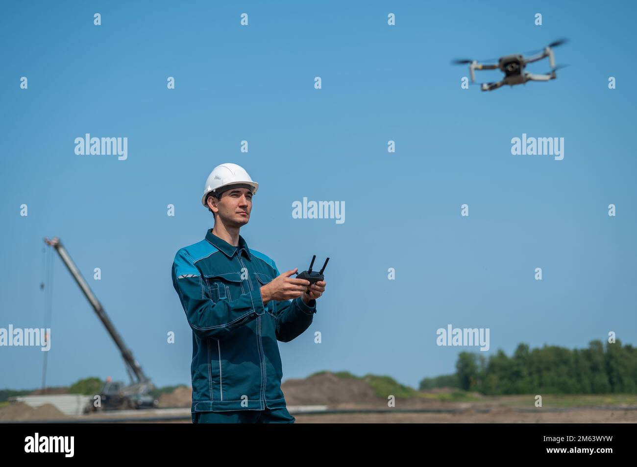 A man in a helmet and overalls controls a drone at a construction site. The builder carries out technical oversight. Stock Photo