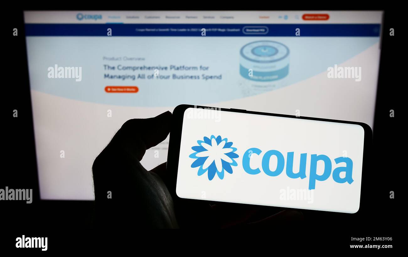 Person holding smartphone with logo of spend management company Coupa Software Inc. on screen in front of website. Focus on phone display. Stock Photo