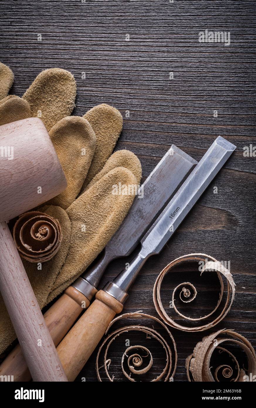 Brown leather gloves flat chisels wooden mallet and planning chips on vintage wood board vertical view construction concept. Stock Photo