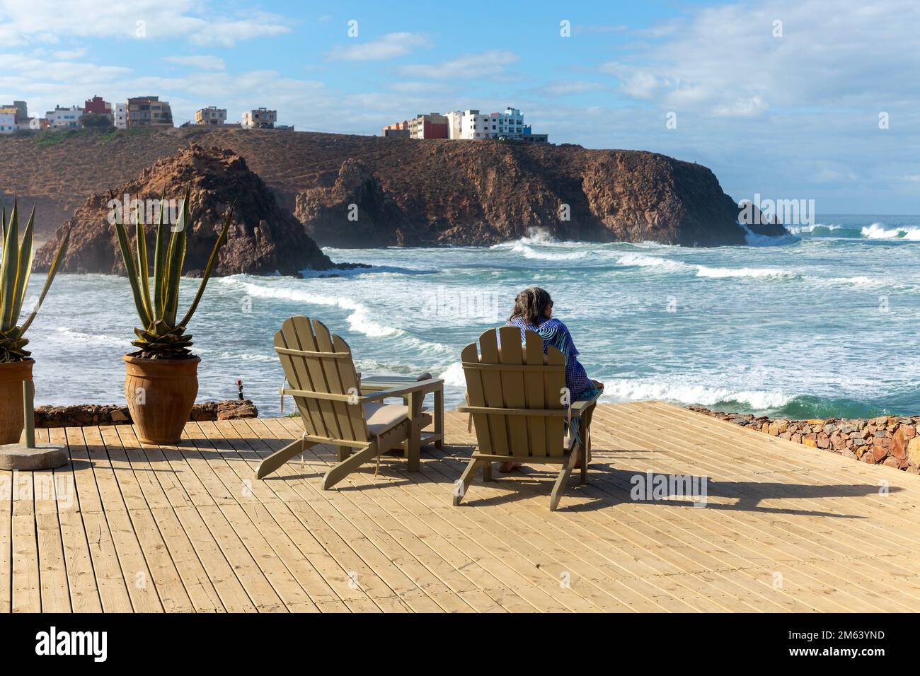 Woman sitting looking out to sea from decking at Hotel auberge Dar Najmat, Mirleft, southern Morocco, north Africa Stock Photo