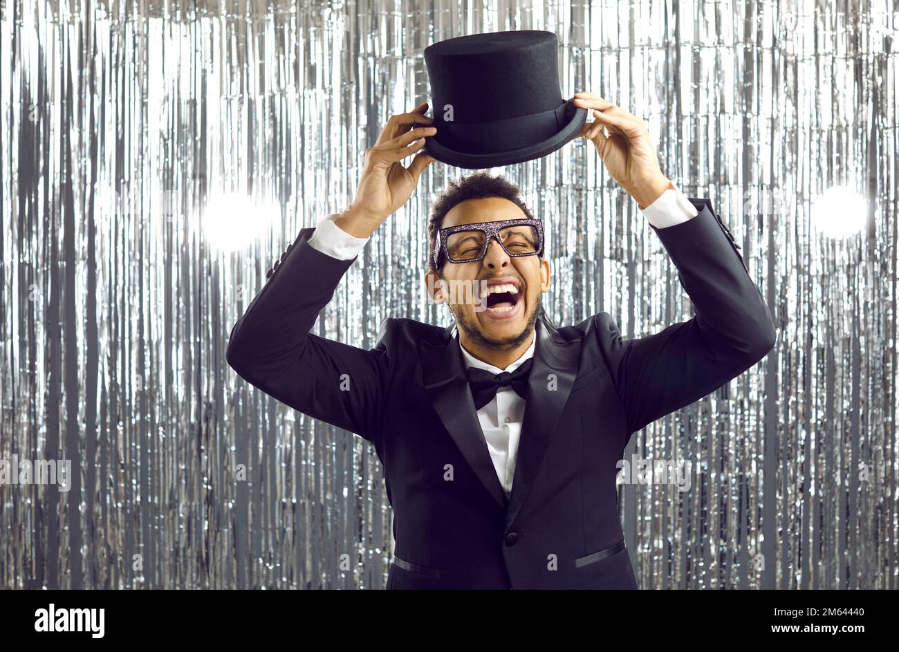 Happy funny black man in a tuxedo suit and top hat laughing and having fun at a party Stock Photo