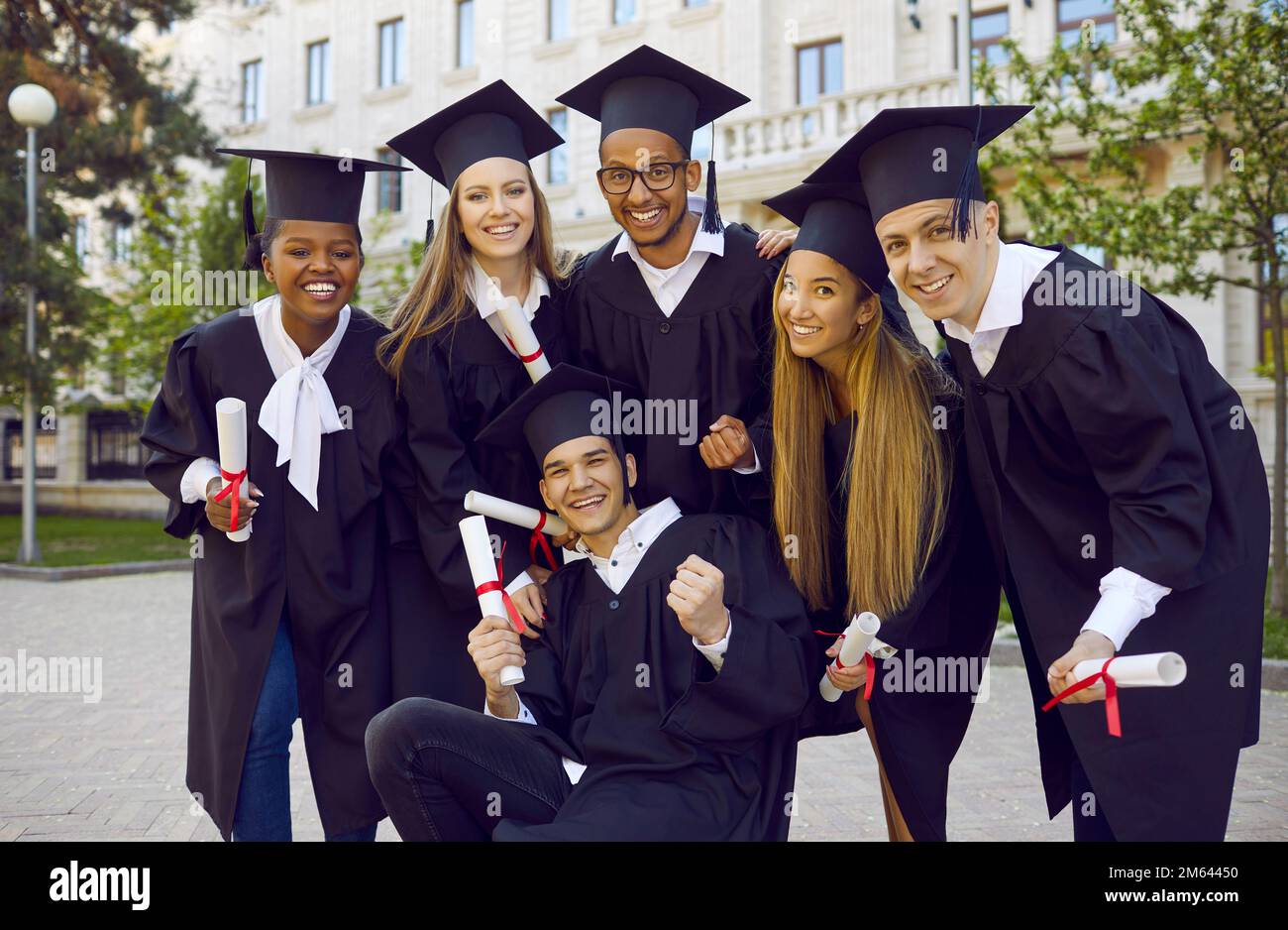 Happy university graduates in academic caps and gowns having fun on graduation day Stock Photo