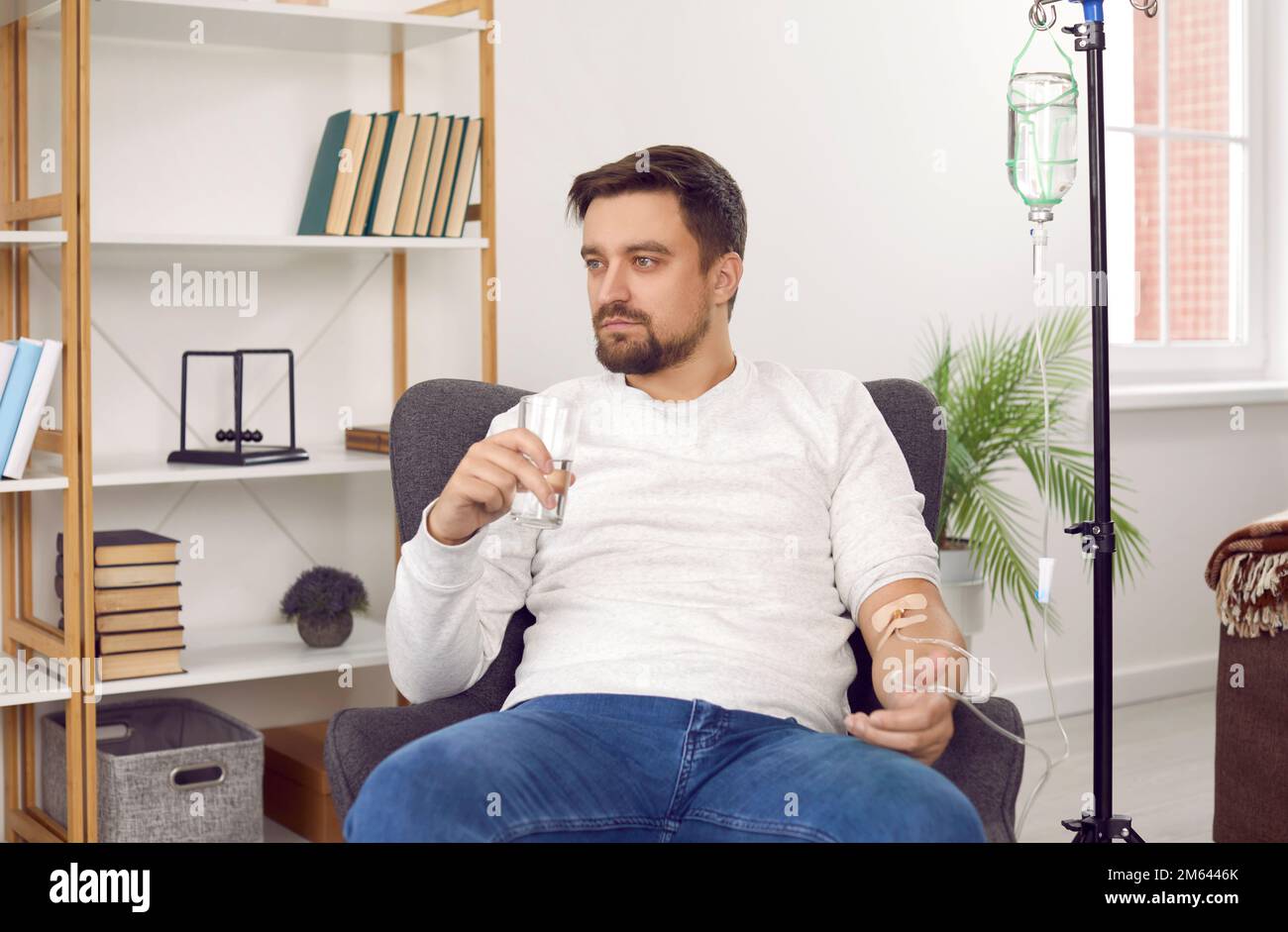 Man sitting in armchair, receiving intravenous infusion and taking medicine with glass of water Stock Photo