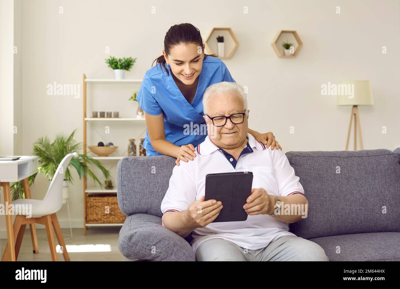 Nurse or caregiver helping happy retired senior man to use modern tablet computer Stock Photo