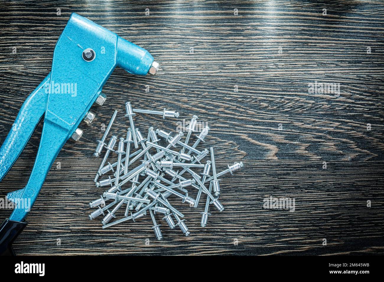 Riveting pliers pile of screws on wooden board. Stock Photo