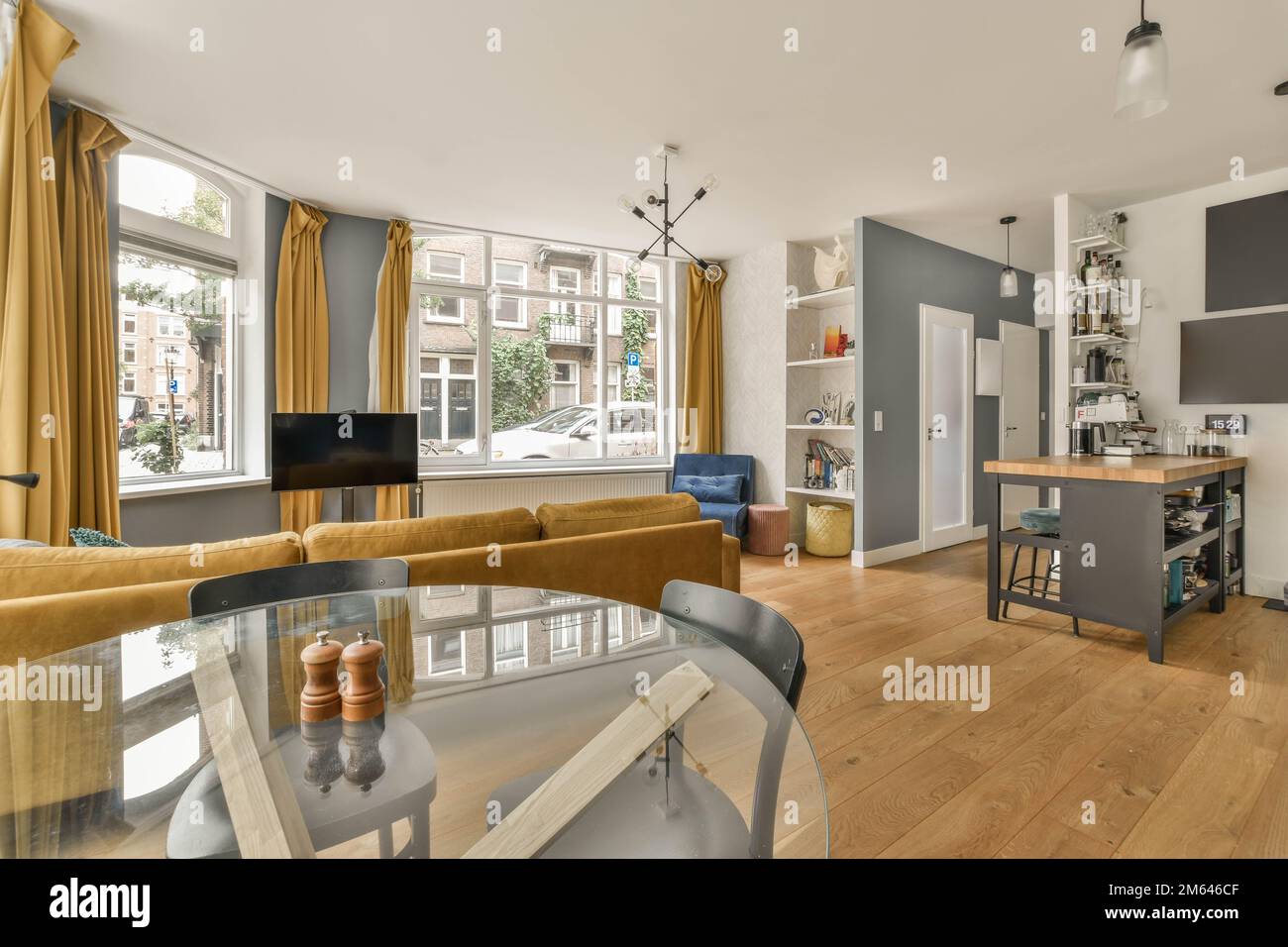 a living room with wood flooring and yellow drapes hanging from the window in the dining area is next to the couch Stock Photo