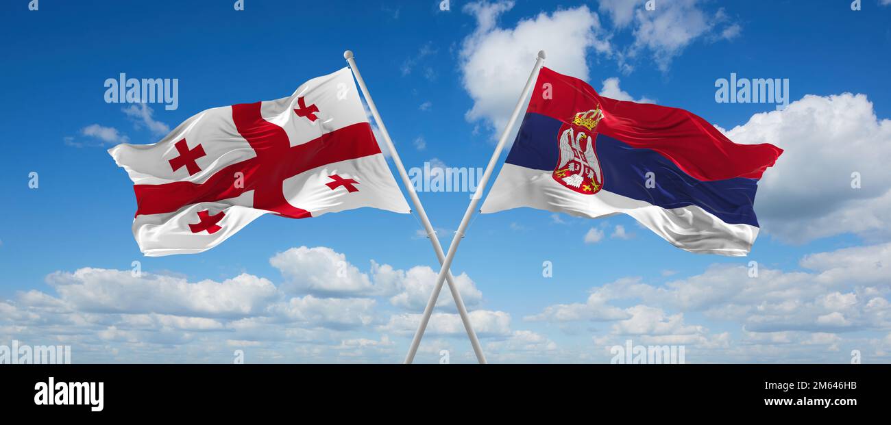 two crossed flags Serbia and Georgia waving in wind at cloudy sky ...