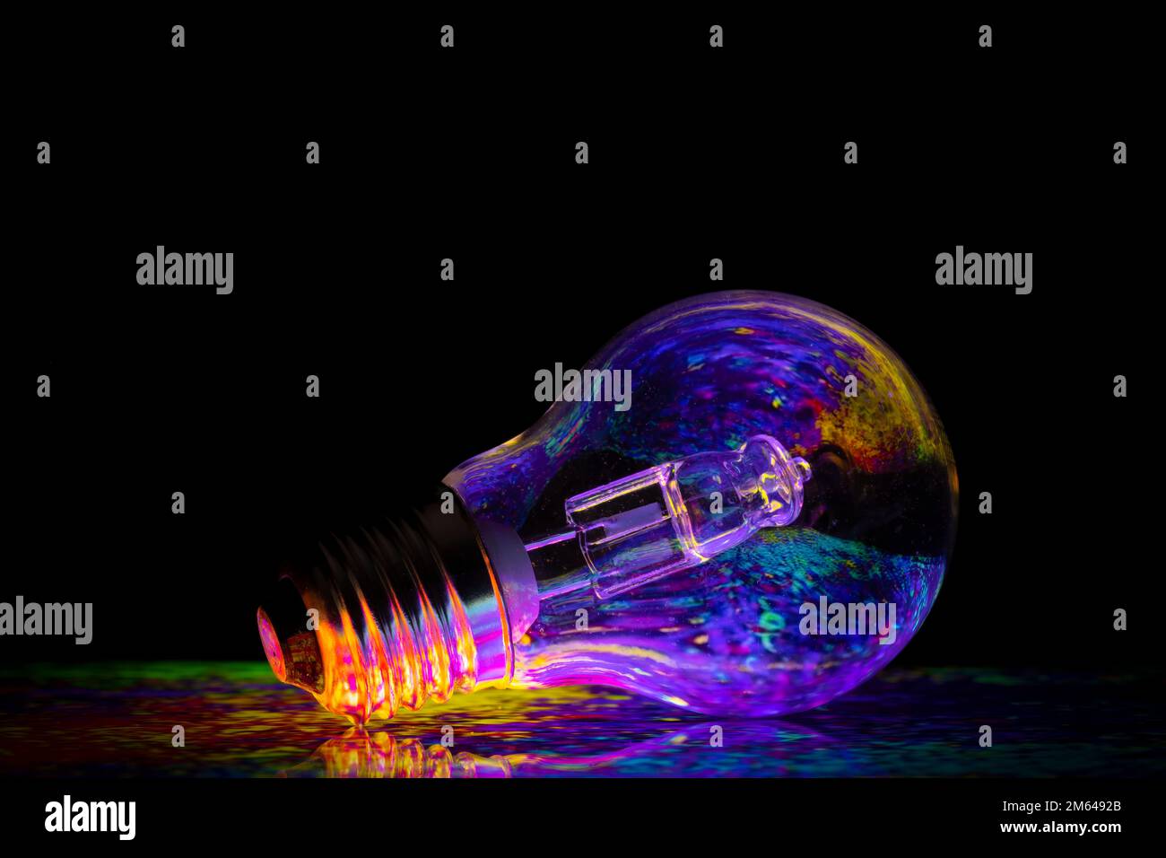 Colourful patterns reflect within a clear glass round shaped lightbulb, photographed against a black background Stock Photo