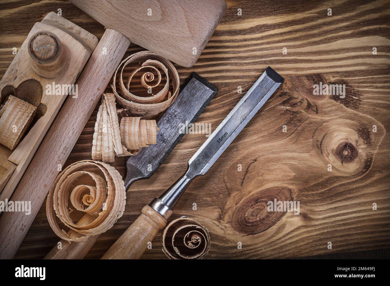Wooden mallet shaving plane flat chisels curled shavings on vintage wood board construction concept. Stock Photo