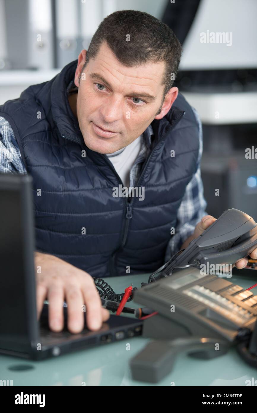 technician looking at laptop while repairing a telephone Stock Photo