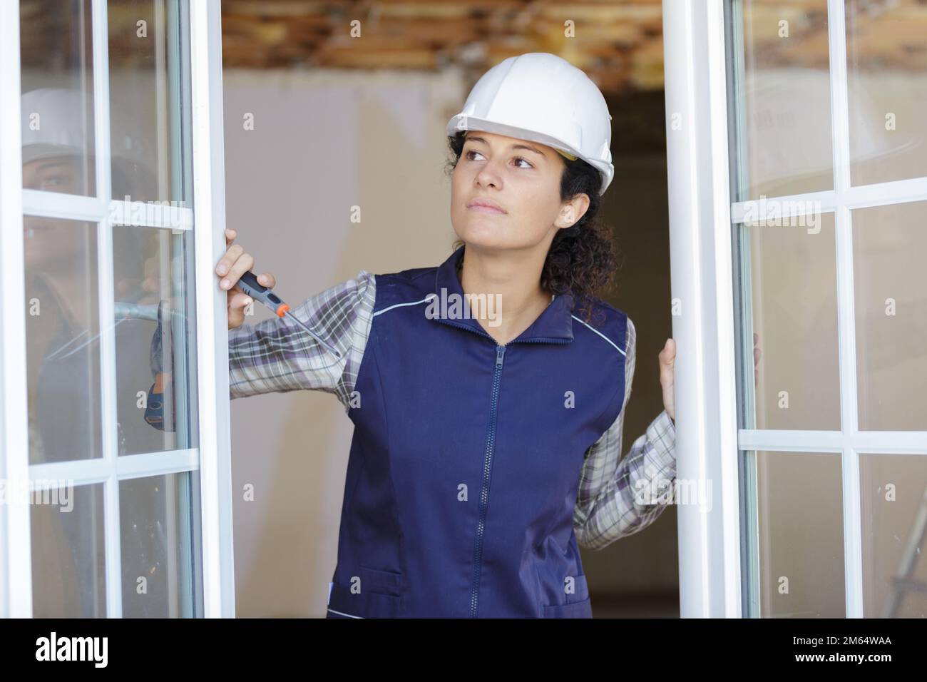 female contractor holding screwdriver looking out from double glazed windows Stock Photo