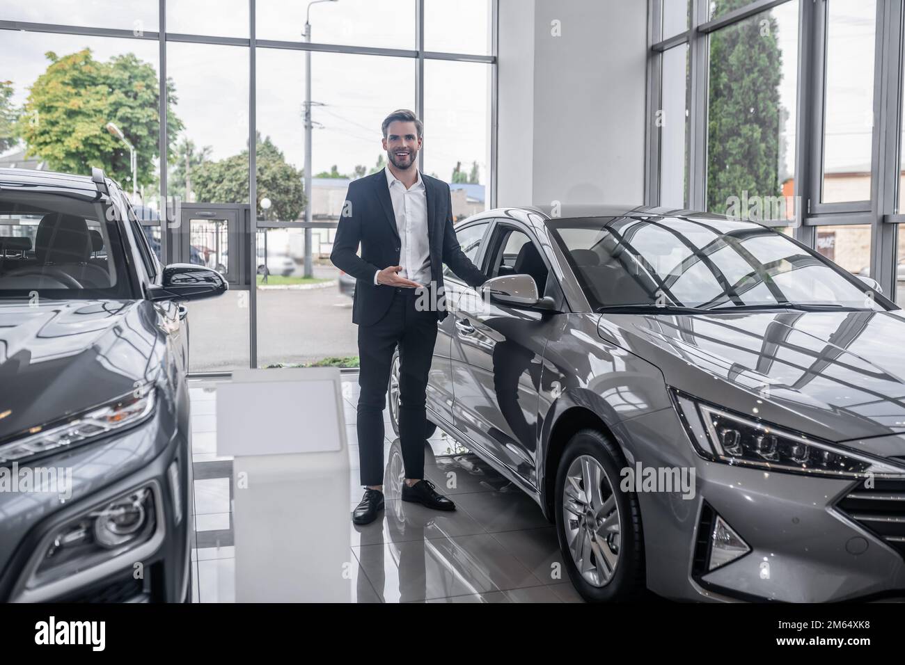 Goodlooking salesperson presenting a new vehicle in a car dealership