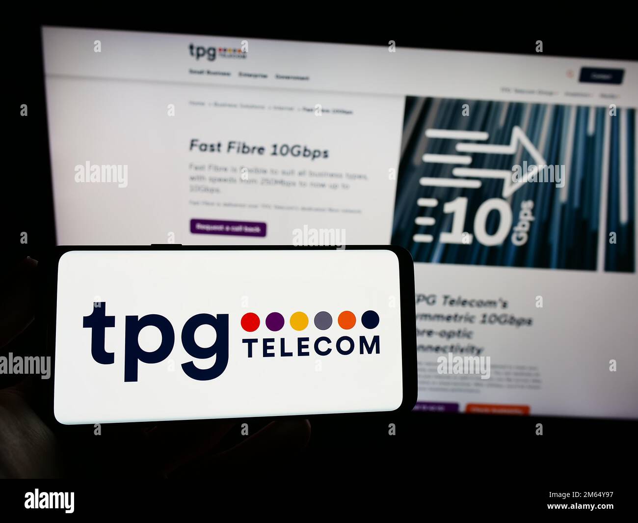 Person holding smartphone with logo of Australian company TPG Telecom Limited on screen in front of website. Focus on phone display. Stock Photo