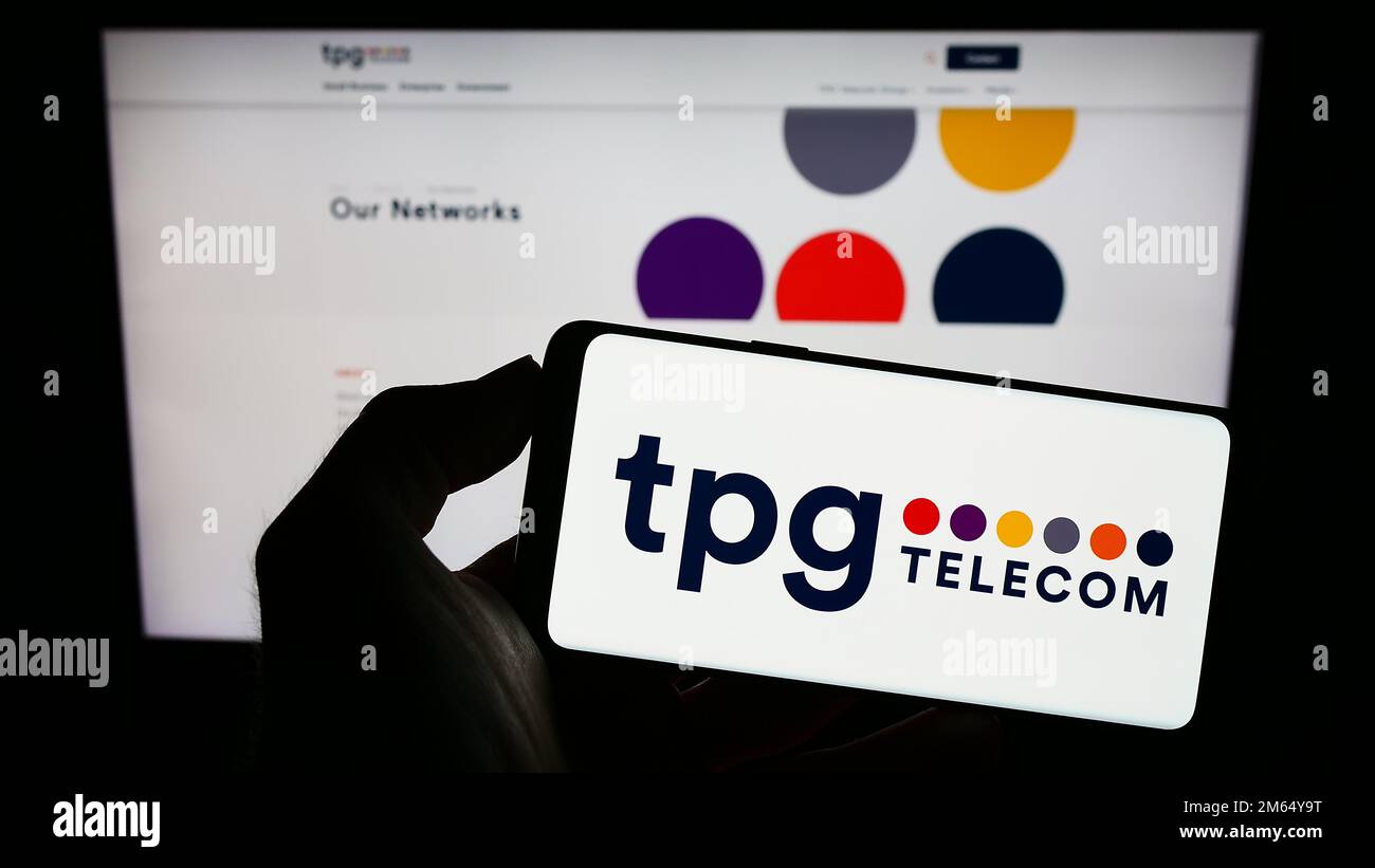 Person holding mobile phone with logo of Australian company TPG Telecom Limited on screen in front of business web page. Focus on phone display. Stock Photo