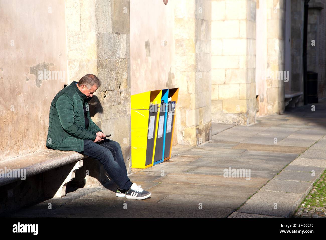 Man sitting on bench checks notifications on smartphone Stock Photo