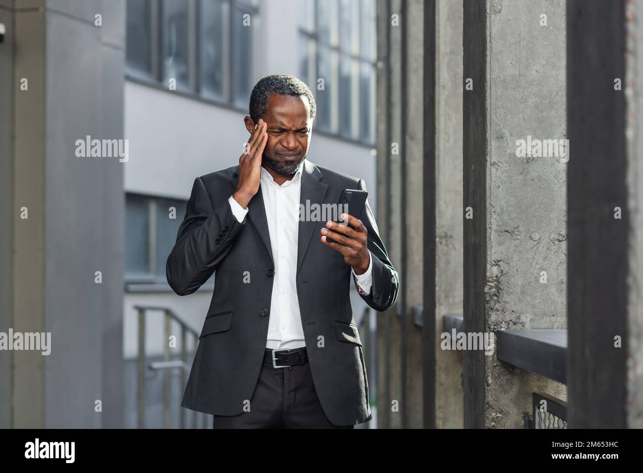 African american boss outside office building with phone in hands reading bad news online, man received notification about money loss and fraud, upset businessman. Stock Photo