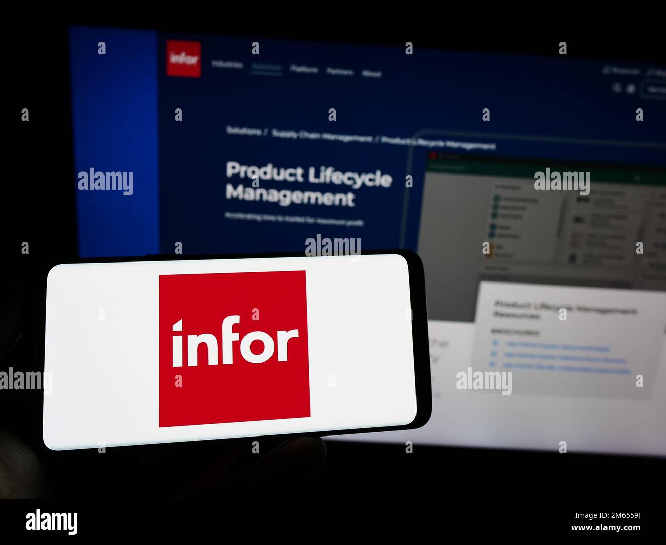 Person holding mobile phone with logo of American enterprise software company Infor on screen in front of website. Focus on phone display. Stock Photo