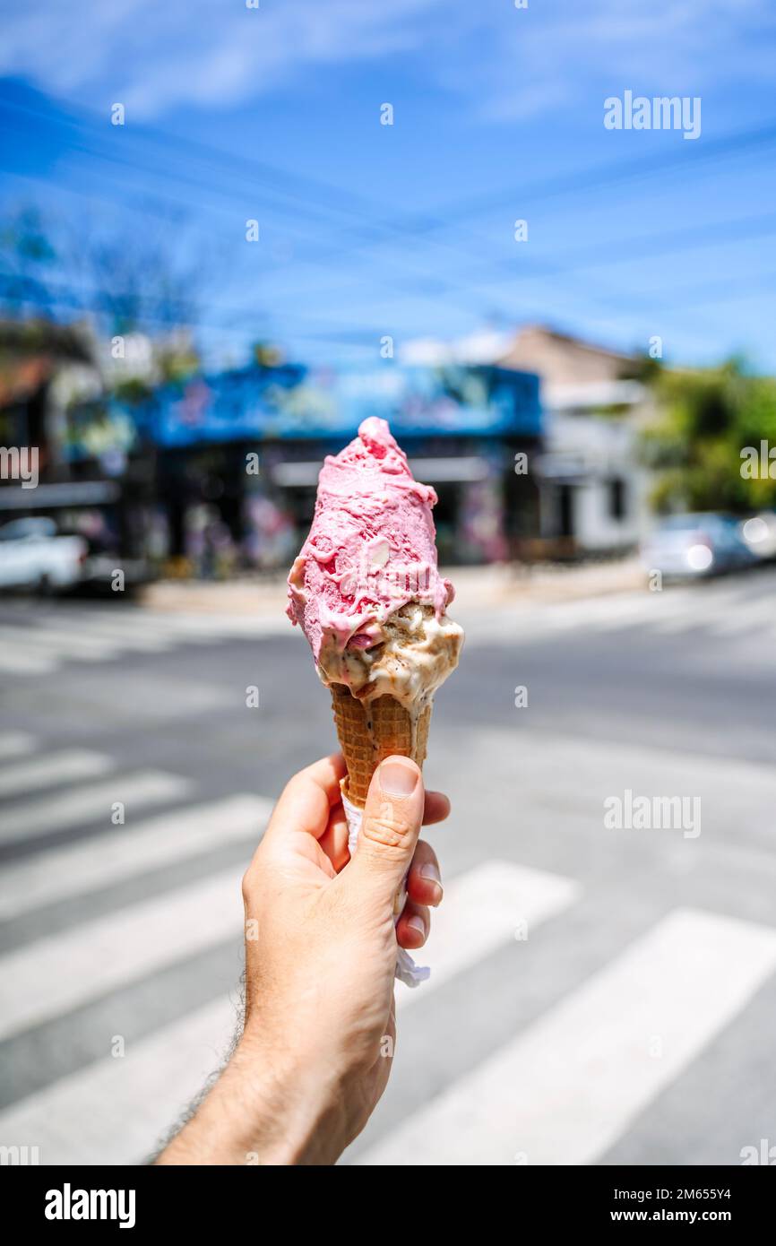 Ice cream in hand. Waffle cone with ice cream on the background of the street in the summer on a hot day. Street food, sweets, desserts concept. High quality photo Stock Photo