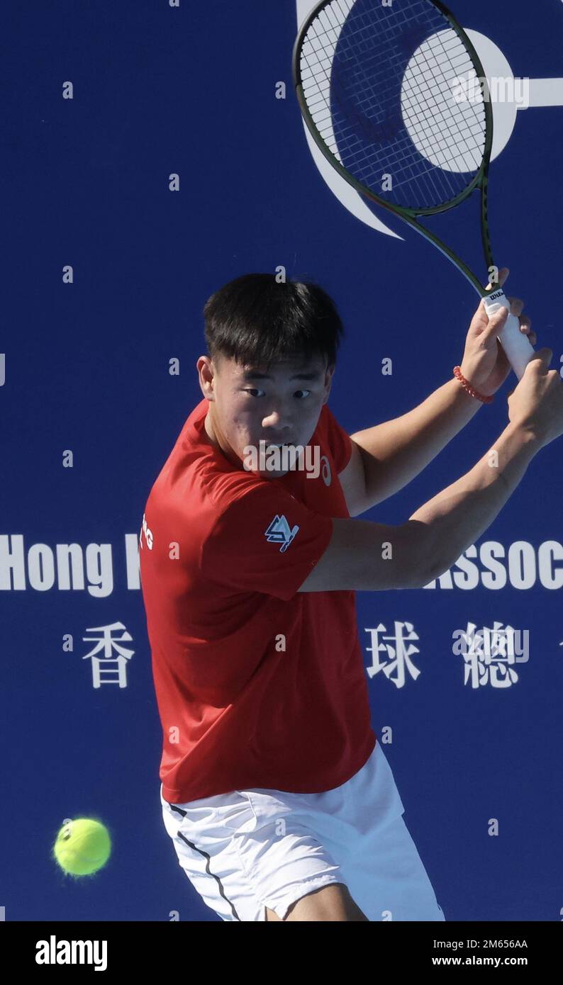 Huang Zelin, wearing a red shirt and white shorts, is preparing to hit a tennis ball during the US Open 2025 in Hong Kong, with a backdrop featuring the Hong Kong Tennis Association branding.